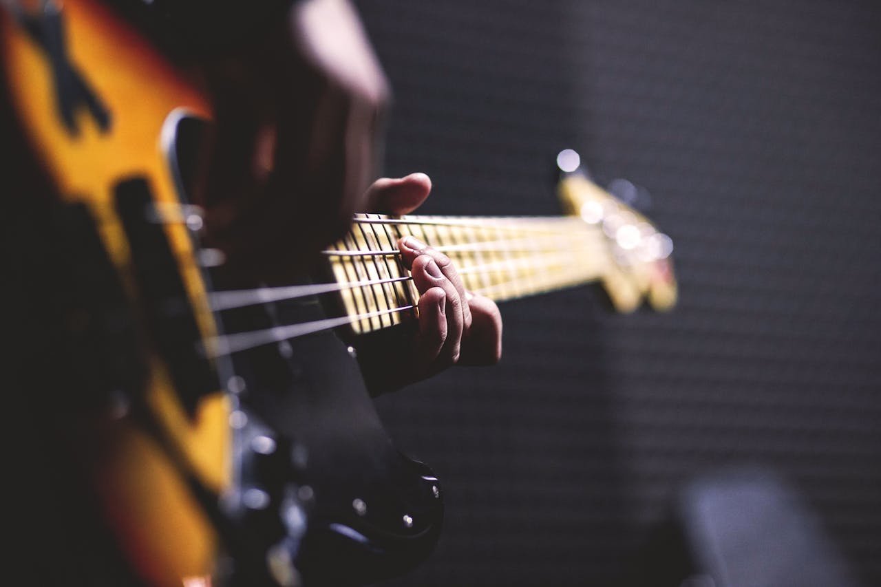 about-us-01 Close-up of a musician strumming an electric bass guitar with focus on fingers.